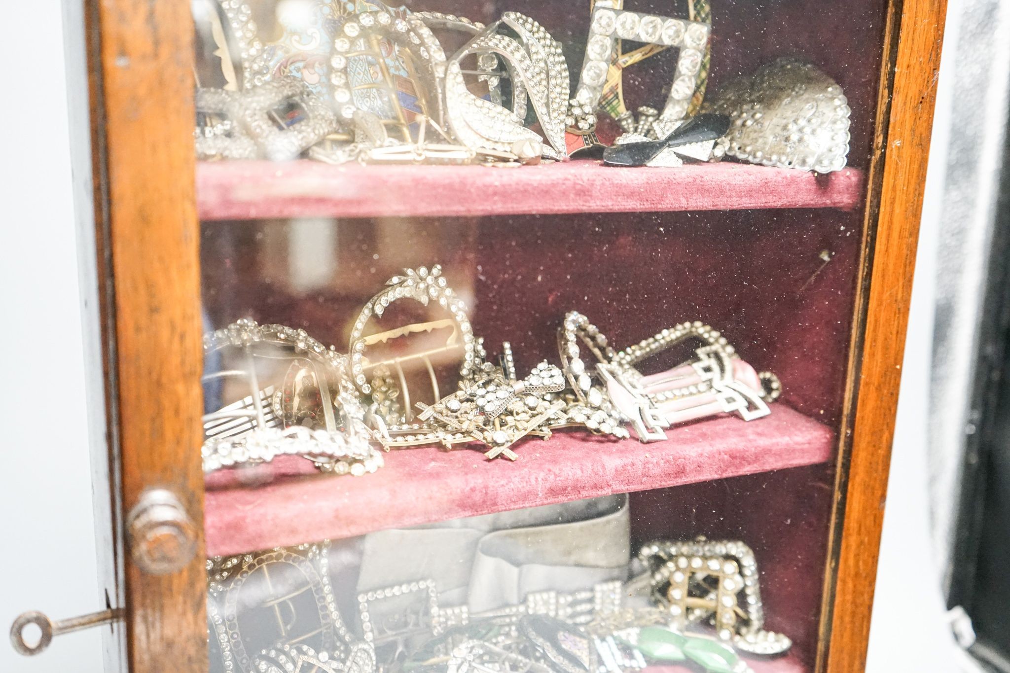 A large collection of 19th/20th century paste and enamel belt and shoe buckles and clips, contained in an oak display cabinet. 56cm